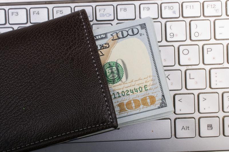 A keyboard with a wallet on top. The wallet has cash peeking out.
