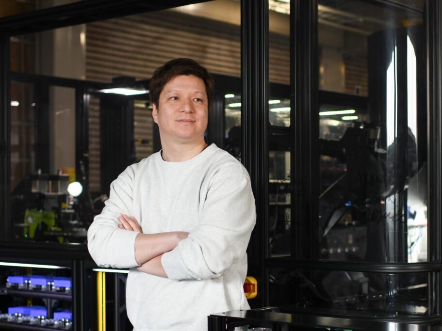 A man in a cream sweater standing in a factory.