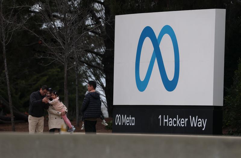 Visitors take pictures by a sign in front of Meta headquarters